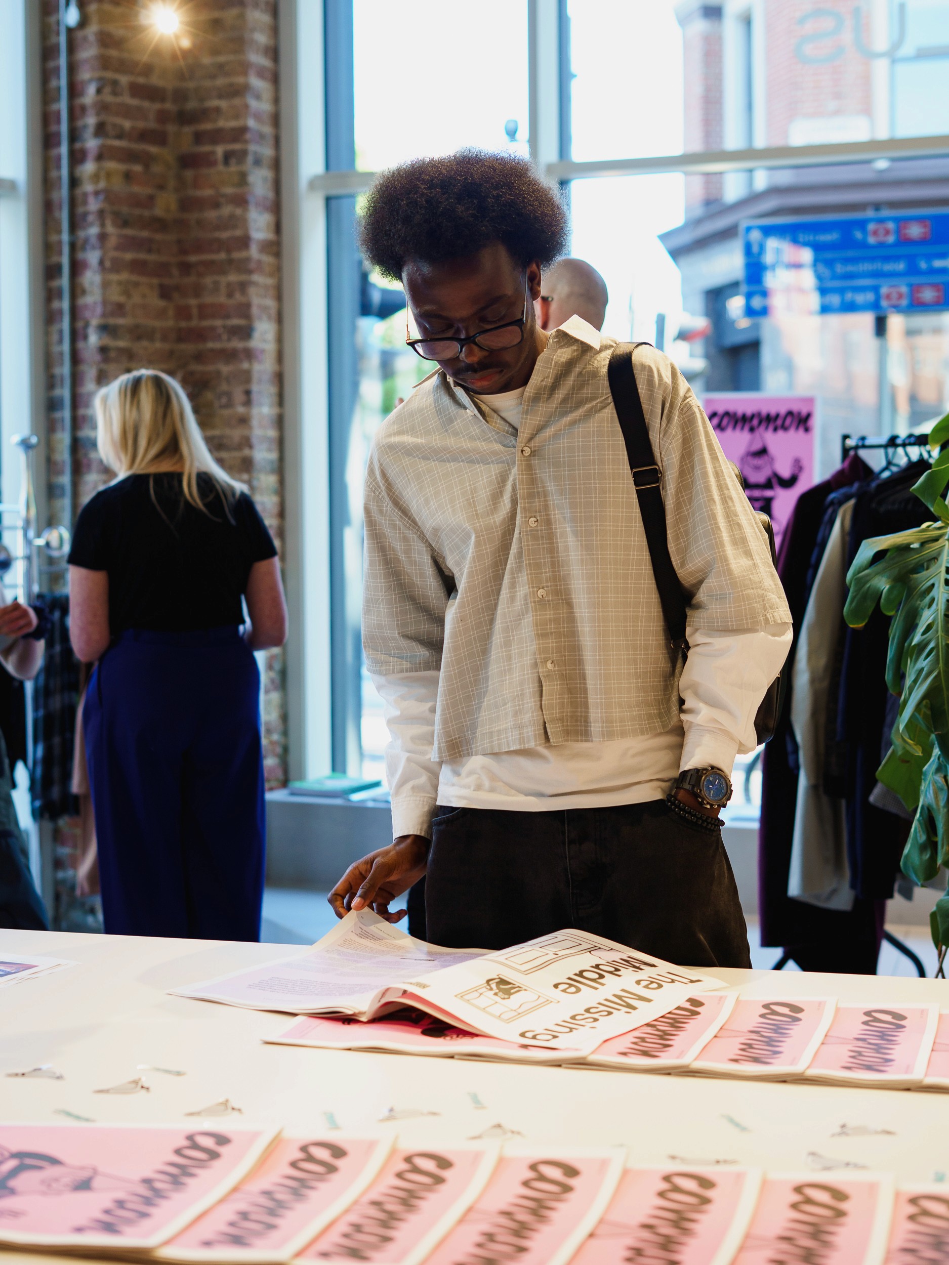 Visitor browsing copies of Common magazine laid out on a table at the launch, with a clothing rail behind