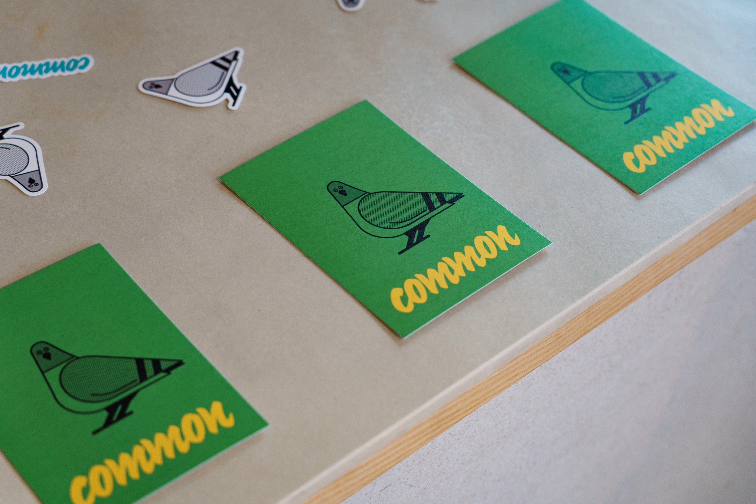 Green Common postcards with a pigeon illustration, laid out alongside pigeon stickers