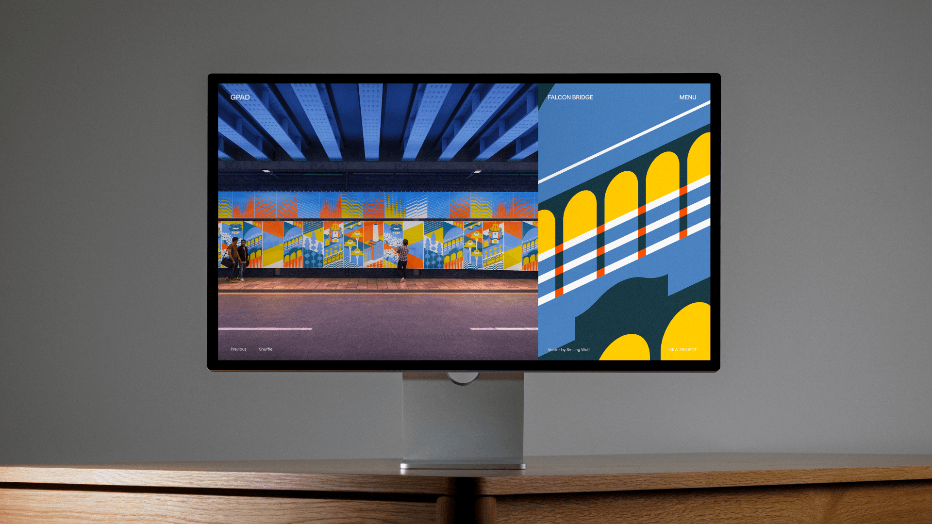 Desktop monitor on a wooden desk showing the GPAD website with a colourful bridge mural