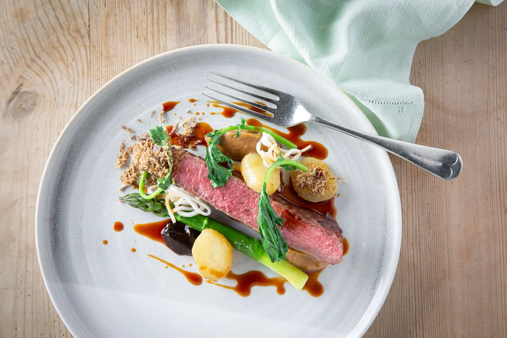 Overhead view of a plated dish of pink-cooked meat with asparagus, potatoes and jus