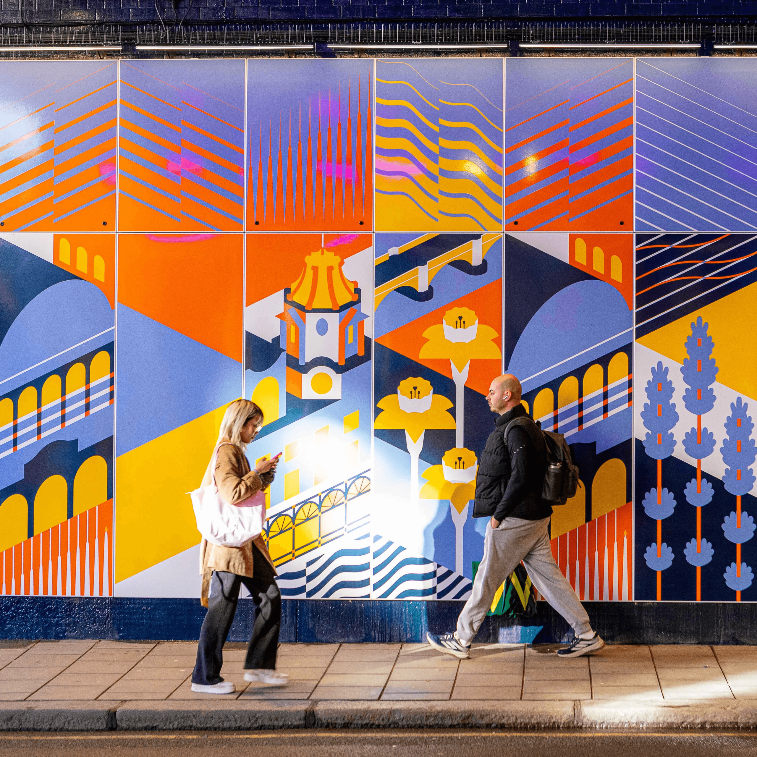 Two people walking past the illustrated Falcon Bridge underpass mural at night