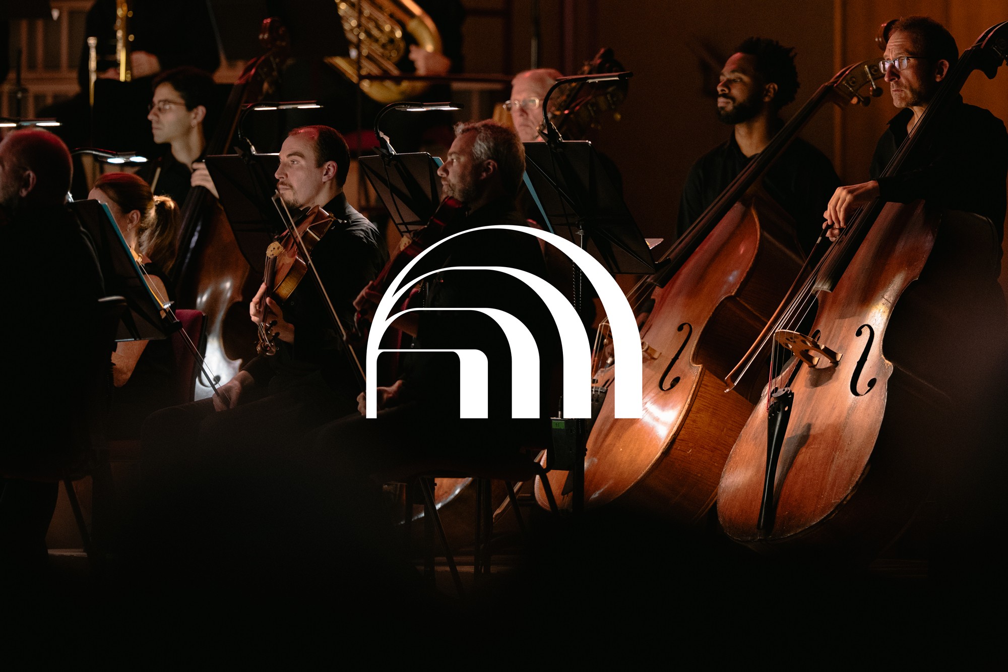 Orchestra string players on a dark stage with the Liverpool Philharmonic arch logo